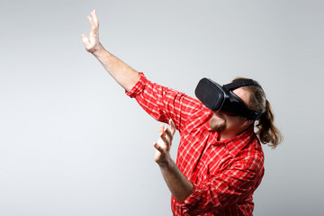 Portrait of bearded man watching virtual reality glasses over gray background with copyspace.