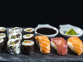 Close up Sushi Set on Slate with Tuna and Salmon Sushis, Sushi Rolls and Wasabi on Black Background