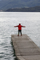 Mann steht auf einem Steg, Mit Jogginghose und Kaputzenshirt begleitet, am Comer See mit ausgebreiteten Armen und blickt nach Colico