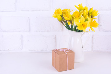 Jar with narcissuses and a gift box at the white background. Spring, mothers day and easter concept