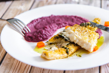 Fried fish, beet puree on a white plate on old boards