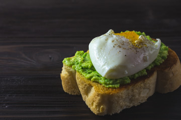 Poached egg on bread toast with smashed avocado. Brown wooden background