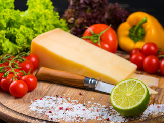 wooden board with parmesan cheese, fresh cherry tomatoes, lettuce, sea salt, lime and red pepper. The knife for cutting vegetables. Appetizing still life from vegetables