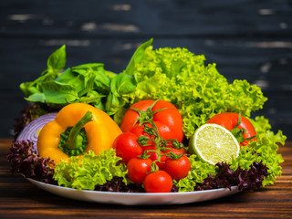 Appetizing still life. Fresh bulgarian yellow pepper, cherry tomatoes, lettuce leaves, red onion, green basil, lime on wooden board.