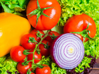 Close up of appetizing still life. Fresh bulgarian yellow pepper, cherry tomatoes, lettuce leaves, red onion, green basil on wooden board.