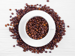 Porcelain white coffee cup and roasted beans on shabby wooden background. Top view.