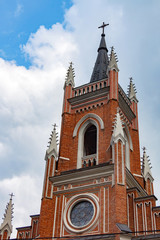 Obraz premium The building of the Catholic church with crosses and the spire on the building on a background of white clouds and a blue sky.
