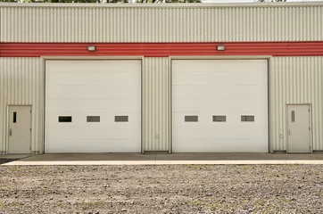 Store enrouleur tamisant sans perçage Bâtiment industriel Entrepôt industriel avec portes roulantes blanches et porte standard des deux côtés.