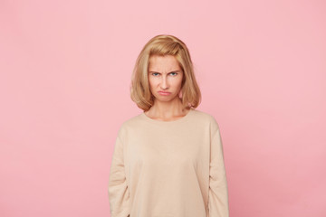 Indoor shot of blonde discontent dissatisfied young woman feels andgry and sinister because offended by her boyfriend. Facial expression and negative emotions. Isolated over pink background