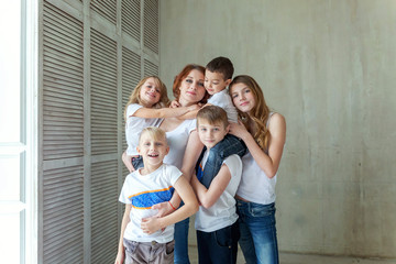 Fototapeta na wymiar Happy family mother and five children near the wall at home. Woman and little kids relax in a white bedroom. Happy family at home. Young mom playing whith their children