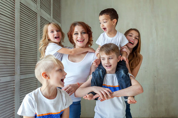 Happy family mother and five children near the wall at home. Woman and little kids relax in a white...