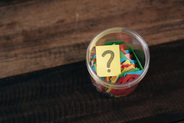 colorful paper with question mark in a plastic jar on wooden table. questions and diversity...