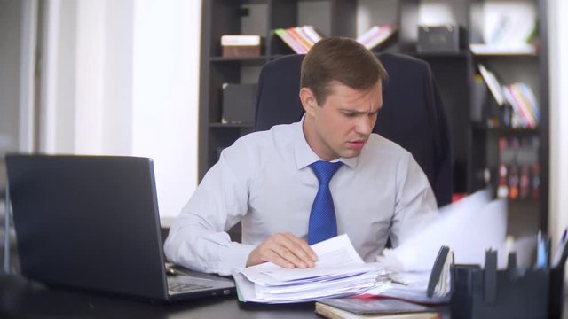 a businessman who scans documents, frowns, using a laptop, does not perform an urgent task in the office, there is not enough time, 4k