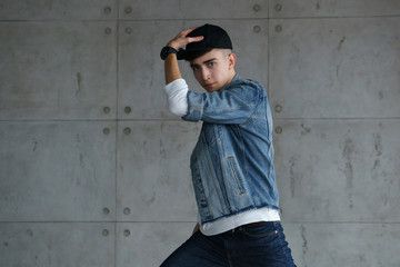 Teenage guy wearing denim jacket and white sweater is dancing hip-hop with baseball cap. Dynamics of modern dance movement. Youth fashion. Close-up portrait