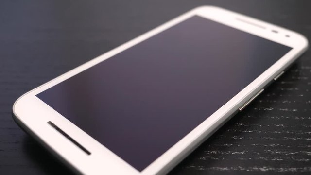 Smartphone with screen turned off on a table with the camera turning around it.
