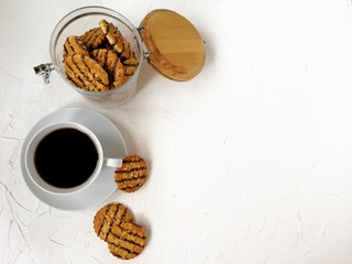 cookies polished with chocolate and peanut pieces in a glass jar with a wooden lid on a light background and against a white brick wall with a Cup of tea
