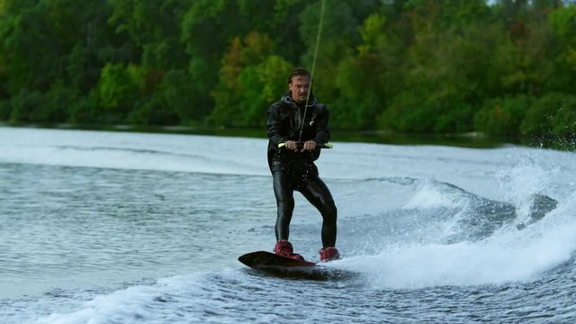 Man wakeboarding on river. Water sport activity in slow motion. Enjoying summer extreme holidays. Stylish man water skiing. Wakeboarder surfing across river. Rider wake boarding boat