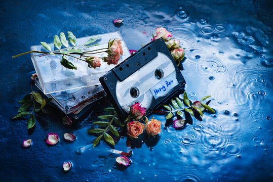 Audio cassette tape with Heavy Rain label in a scene with rose petals and raindrops. Melancholy music for rainy weather. Nostalgia concept copy space.