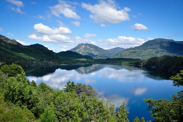 Horizontal photo of lake Machonico in Argentina with water reflection on the foreground and mountains and clouds in the background