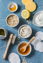 Fototapeta premium Homemade beauty products concept. Natural moisturizing, nourishing, cleansing face mask - coconut oil, oatmeal, natural yogurt, vitamin E, honey, face brush, sponge on blue background, top view