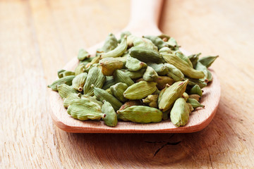 Green cardamom pods on wooden spoon