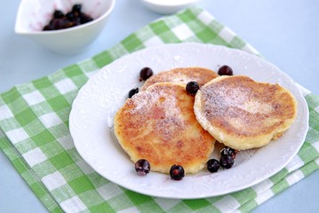 Breakfast. Curd cheese cakes with sour cream and currants sprinkled with powdered sugar.