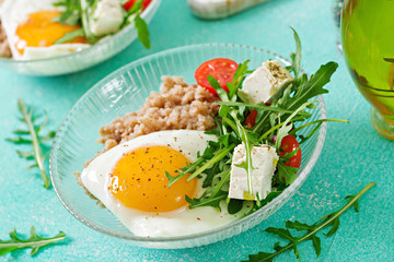 Healthy breakfast with egg, feta cheese, arugula, tomatoes  and buckwheat porridge on light background. Proper nutrition. Dietary menu.