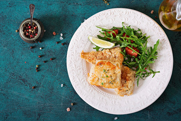 Fried white fish fillets and tomato salad with arugula. Top view