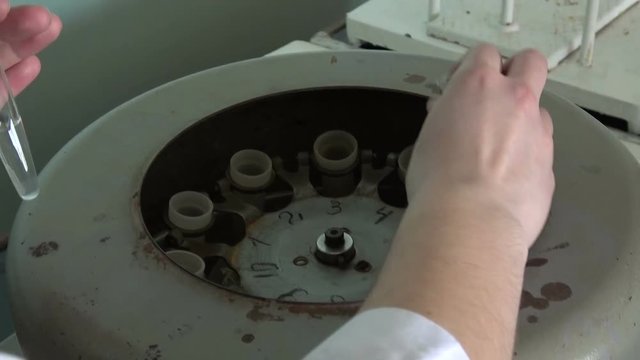 A scientist in a white coat opens a centrifuge in the laboratory