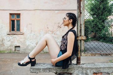 Fototapeta na wymiar A young pretty girl sitting on a fence wall and thinking