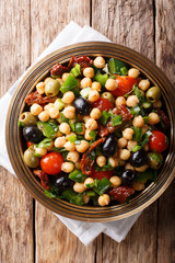 Delicious and dietary salad balela with chickpeas, tomatoes, onions, olives and herbs close-up. Vertical top view