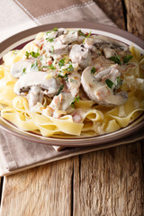 Pasta fettuccine with cream, mushrooms, bacon and onions close-up on a plate on a table. vertical