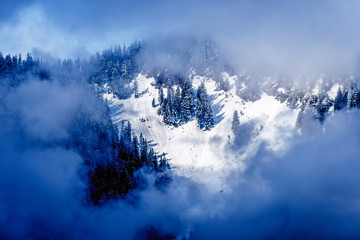 Sun shining through the clouds on the Snow Capped Peak of Coquitlam Mountain in the Coast Mountain Range seen from the shore of Pitt Lake in the Fraser Valley of British Columbia, Canada
