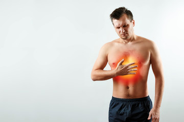 A man holds his hands and region of the heart, chest pain, a pain in the heart highlighted in red, a heart attack. Light background. The concept of medicine, massage, physiotherapy, health.