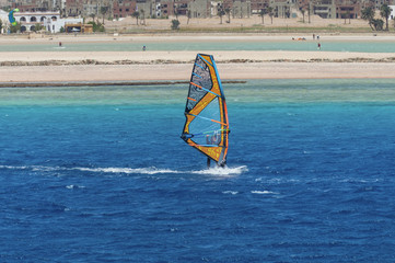 the windsurfer on the board under sail moves at a speed along the surface of the sea,