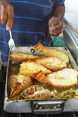 Hand holding forks inverted lobster roasting in oil
