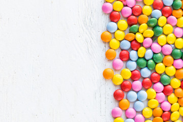 Obraz premium Colorful round candies on white rustic wooden background with copy space. Different Small colored candies. Top view..
