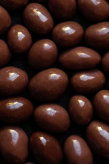 Chocolate candy textured background.  Dark brown chocolate round candies on black concrete background  top view, close up.