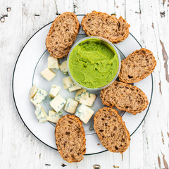 Guacamole, cheese and slices of bread over white wooden background with copy space. Picnic, lunch or dinner concept. Food and drink, top view