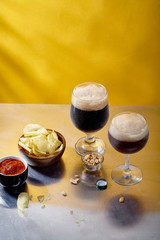 Ale and stout beer in glasses with snacks and sauce on metallic and yellow background