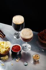 Ale and stout beer in glasses with snacks and sauce on metallic and black background