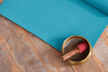 A diverse ethnic objects for meditation and relaxation: singing bowl, blue yoga or fitness mat on wiiden floor in yoga class