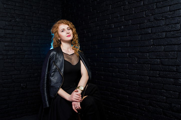 Curly hair girl at leather jacket on studio against black brick wall.