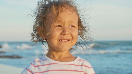 Facial portrait of beautiful little girl standing on the beach and smiling