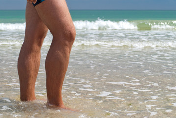 young man feet close-up swimming trunks walking sea shore, wave horizon water, summer rest beach weekend vacation