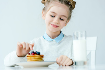 selective focus of little kid looking at homemade pancakes with berries and honey on table