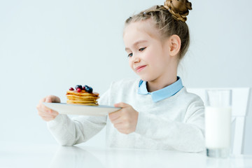 little kid looking at homemade pancakes with berries and honey in hands