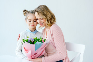 portrait of smiling mother hugging little daughter with beautiful bouquet of flowers, happy mothers day concept
