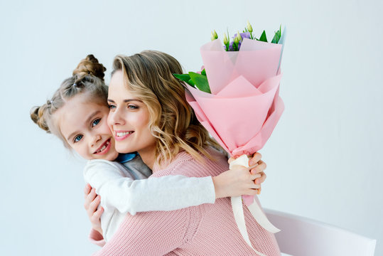 portrait of smiling daughter with bouquet of flowers and happy mother hugging each other, happy mothers day concept