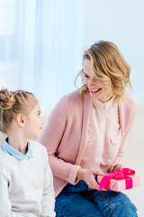 smiling mother holding gift box and looking at daughter on happy mothers day